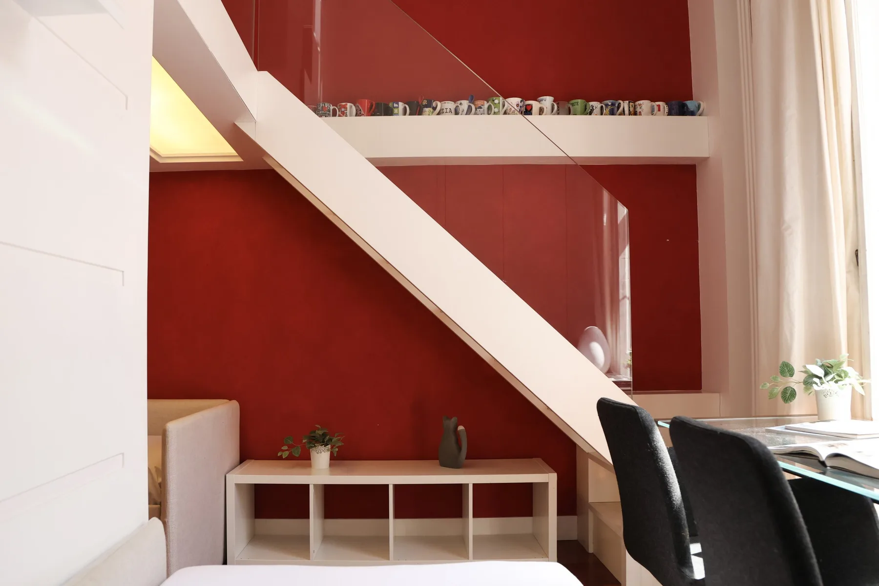 A red-walled room with a diagonal staircase and a low table beneath it.