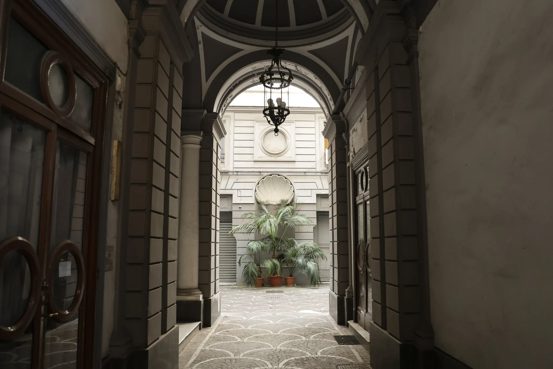 An arched passage opens onto a bright courtyard with potted plants.