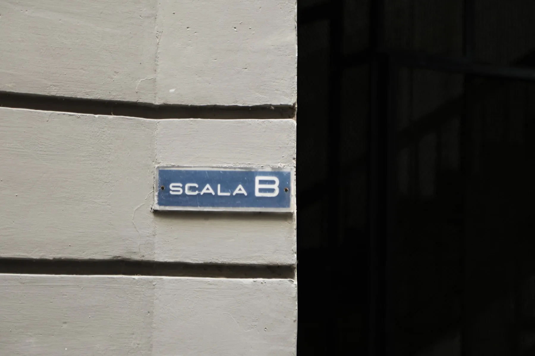 A building entrance with a blue sign marked “Scala B” beside a dark doorway.