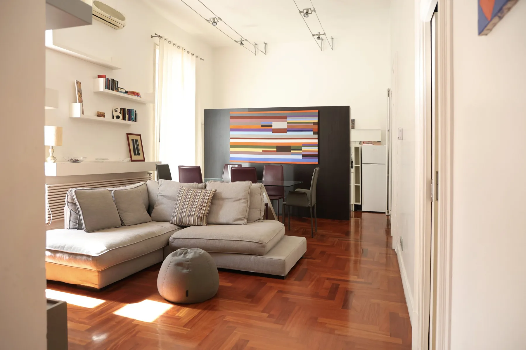A bright living room with sectional seating, wall shelves, and colorful artwork.