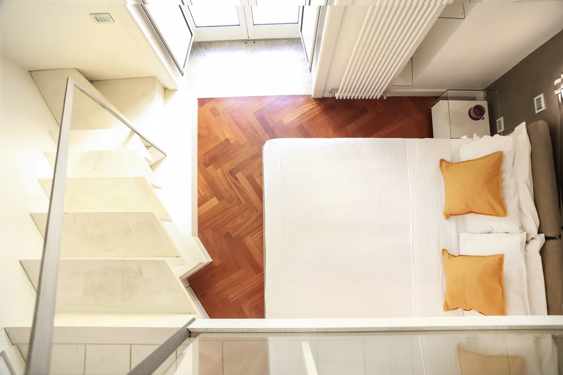 A bedroom with a bed beside a staircase and a window.