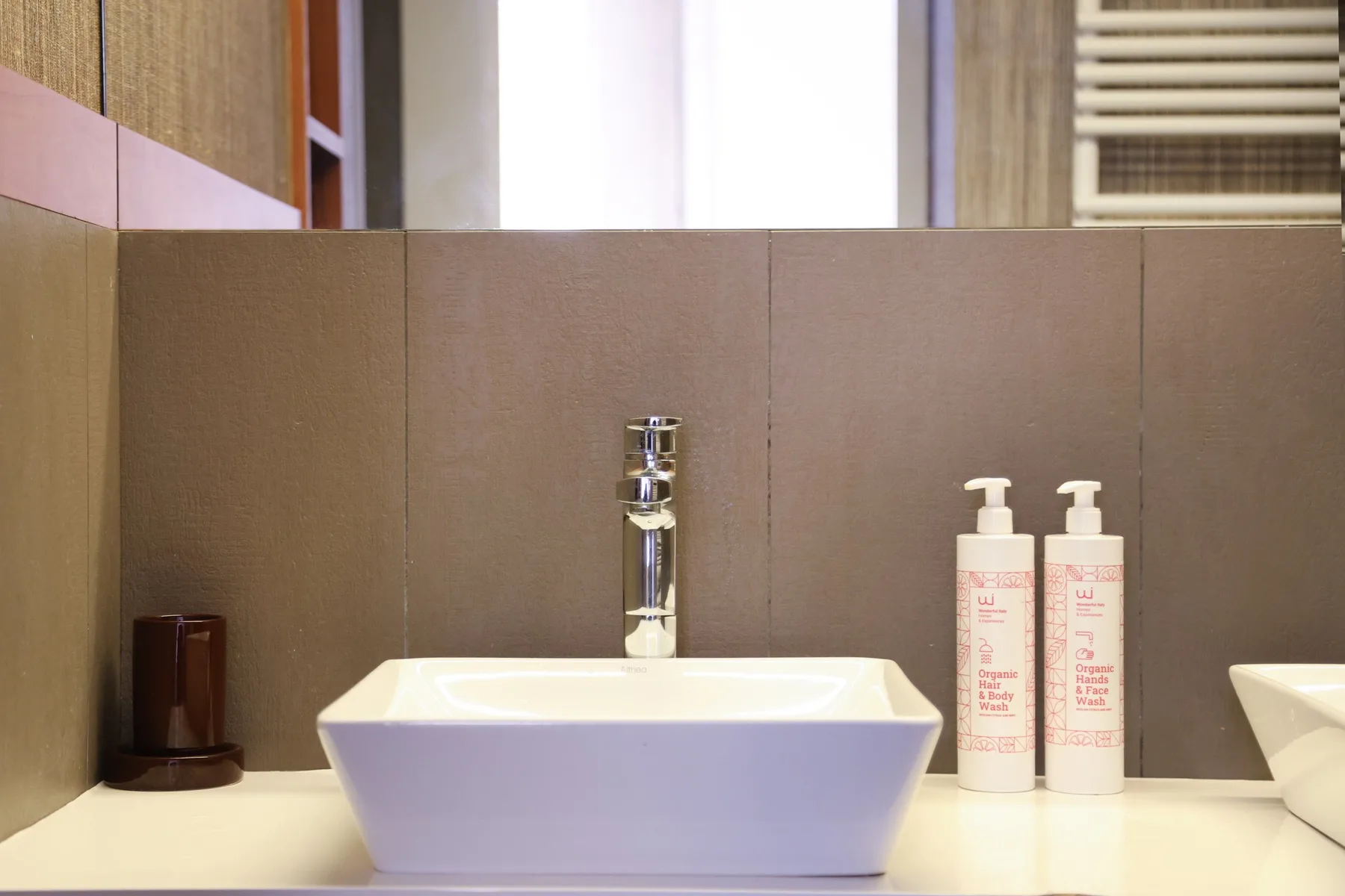 A bathroom vanity features a white vessel sink, chrome faucet, and two pump bottles.