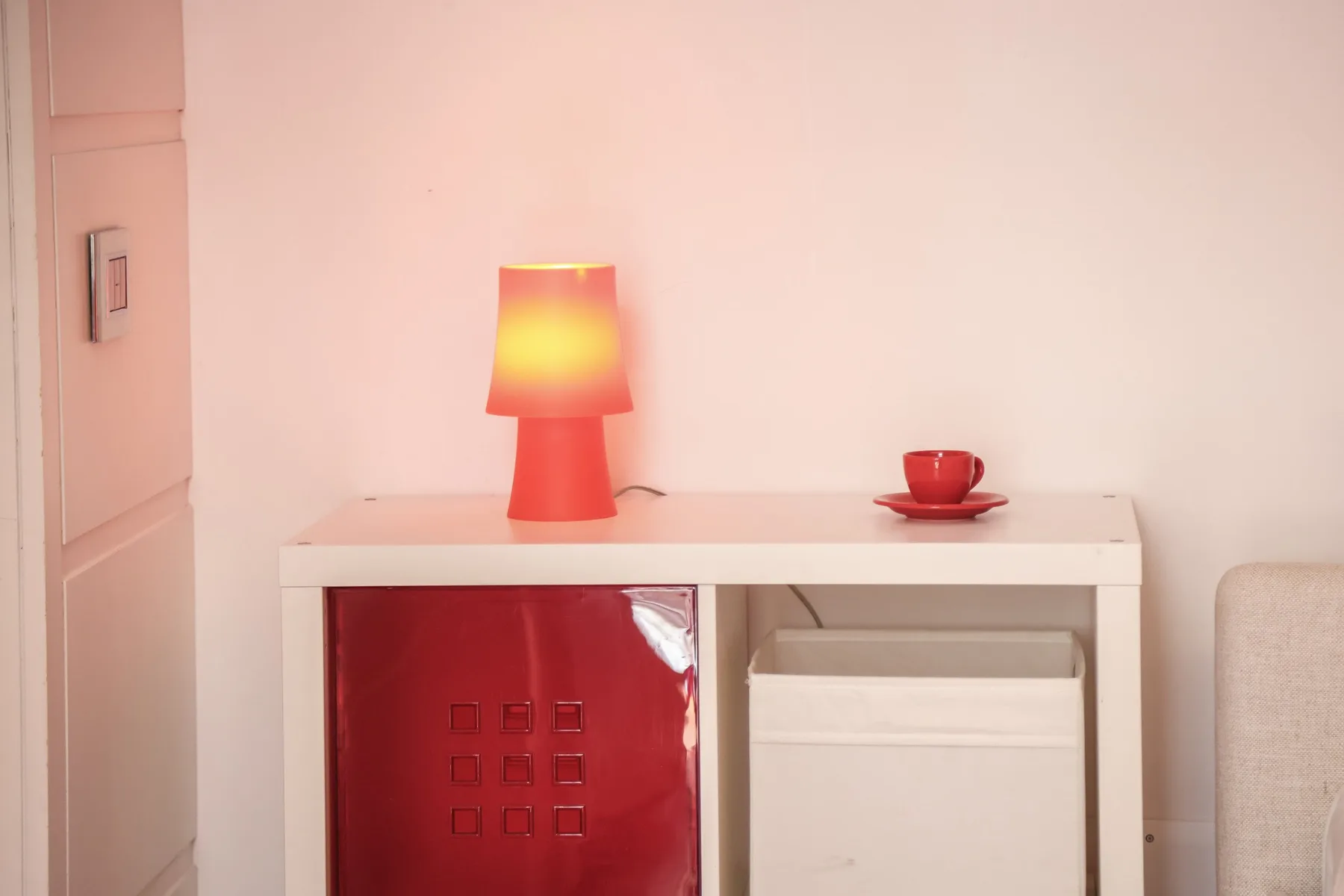 A small table holds a glowing lamp and a red cup beside a cabinet.