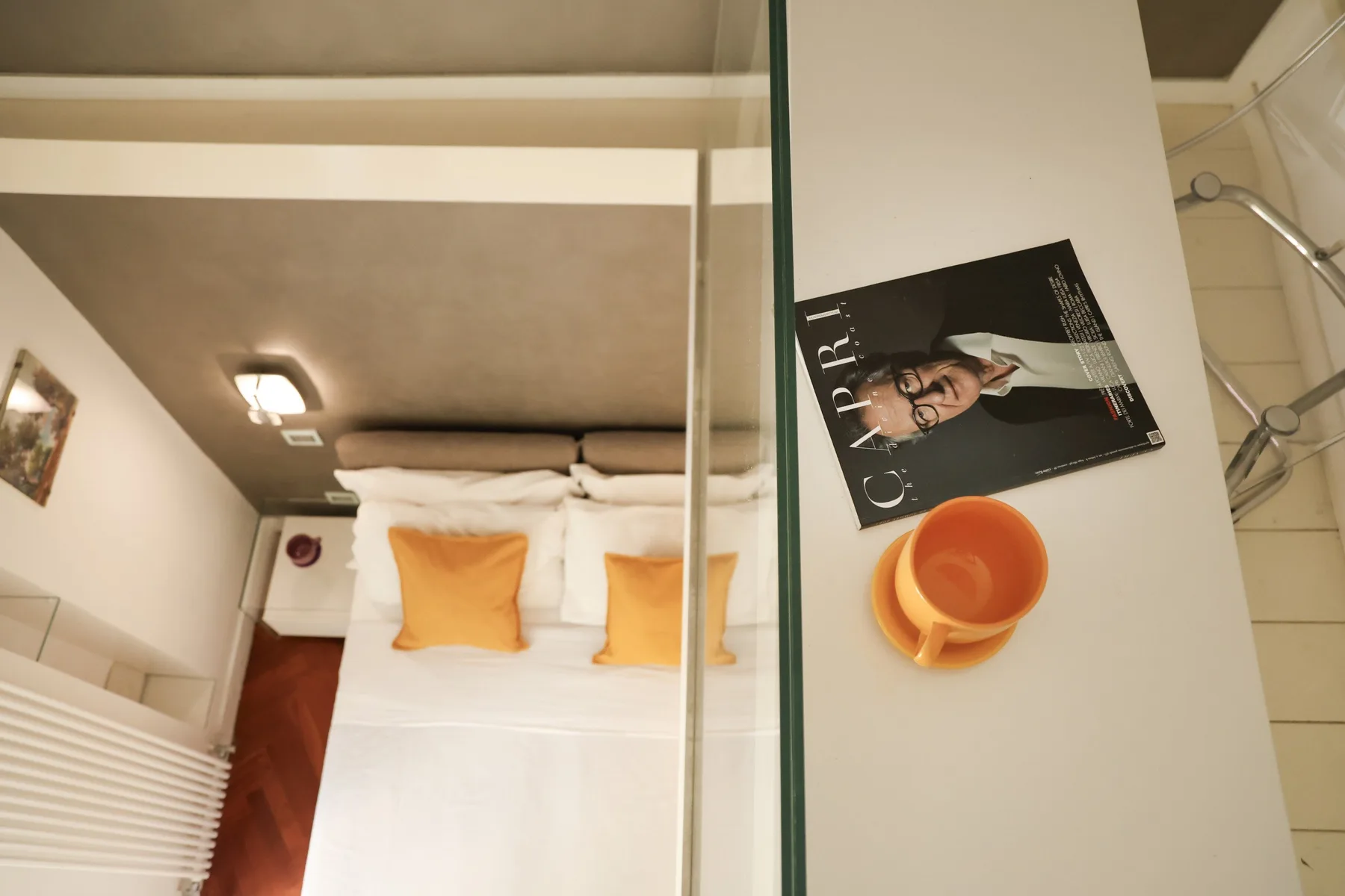 A bedroom with a neatly made bed and orange pillows beside a bathroom counter.