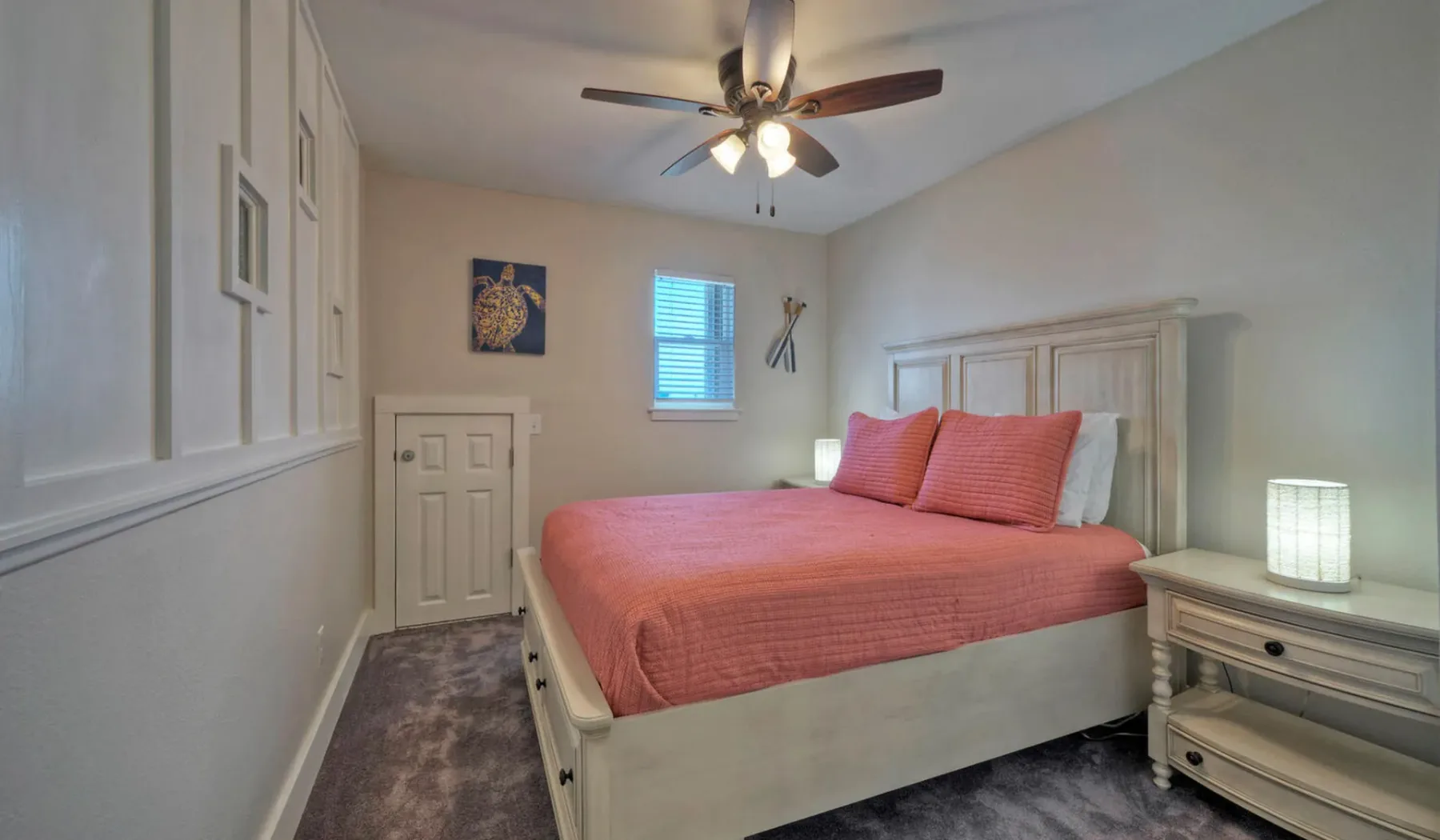 Un dormitorio con una colcha color coral y un ventilador de techo.