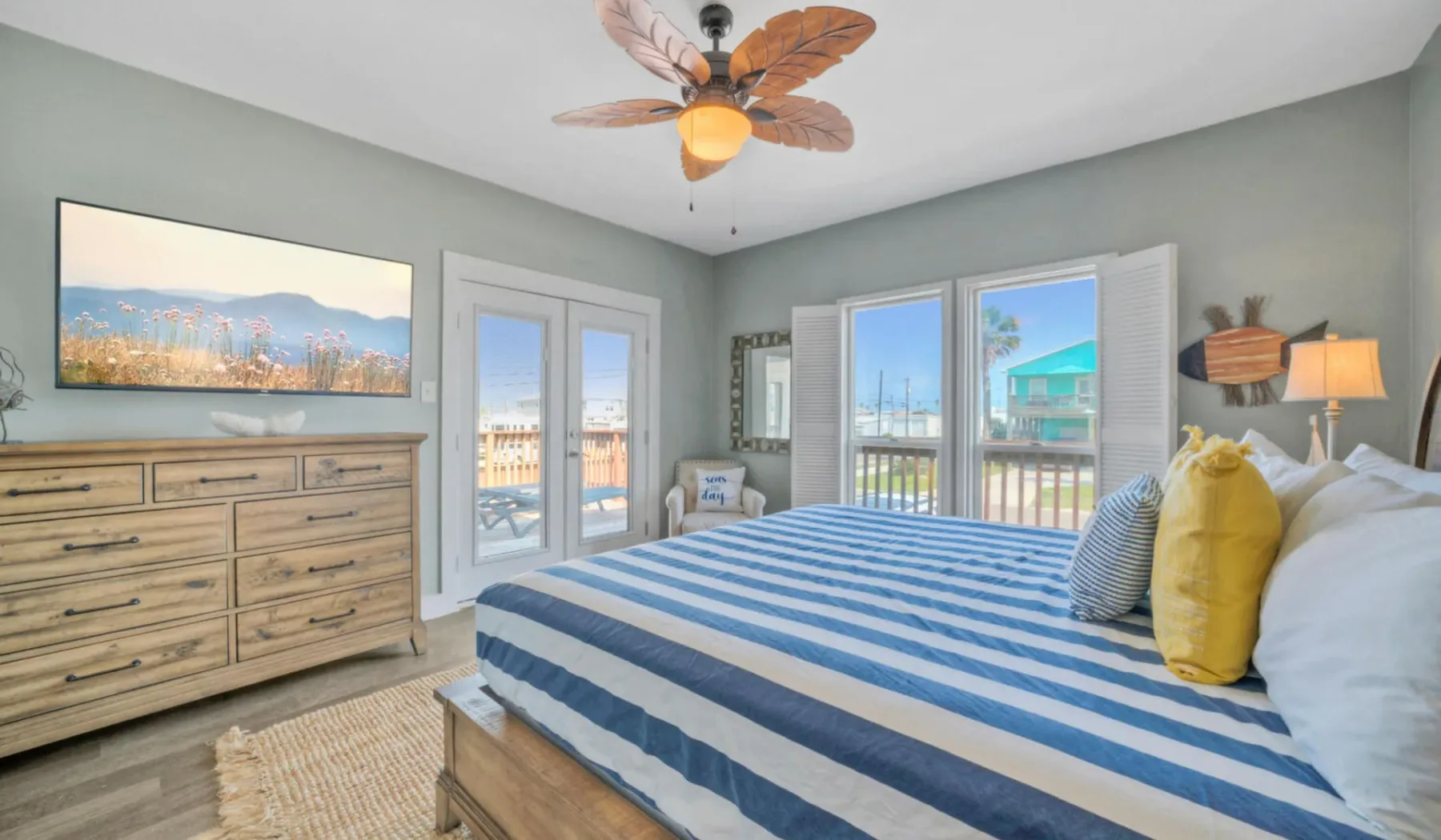 Un dormitorio luminoso con una colcha a rayas azules y blancas y ventanas grandes.
