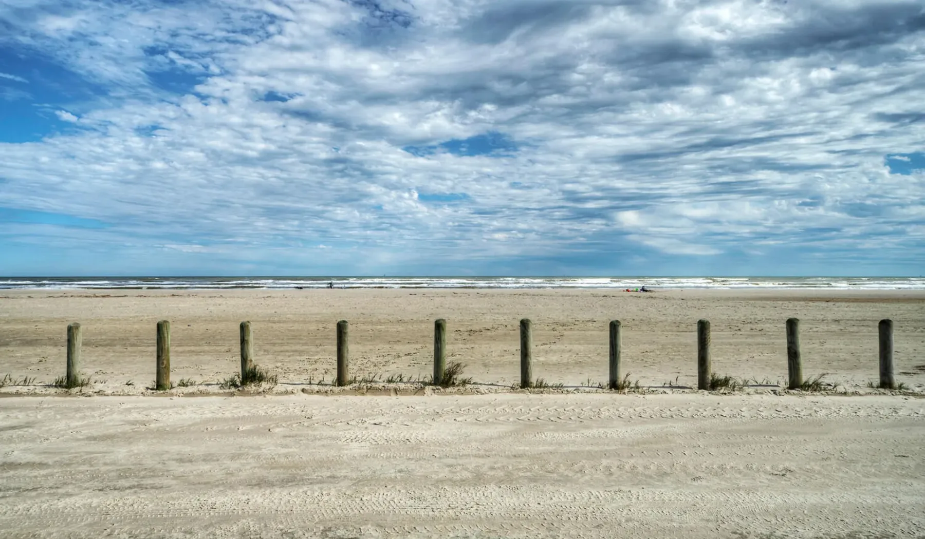Una amplia playa de arena se extiende bajo un cielo azul nublado.