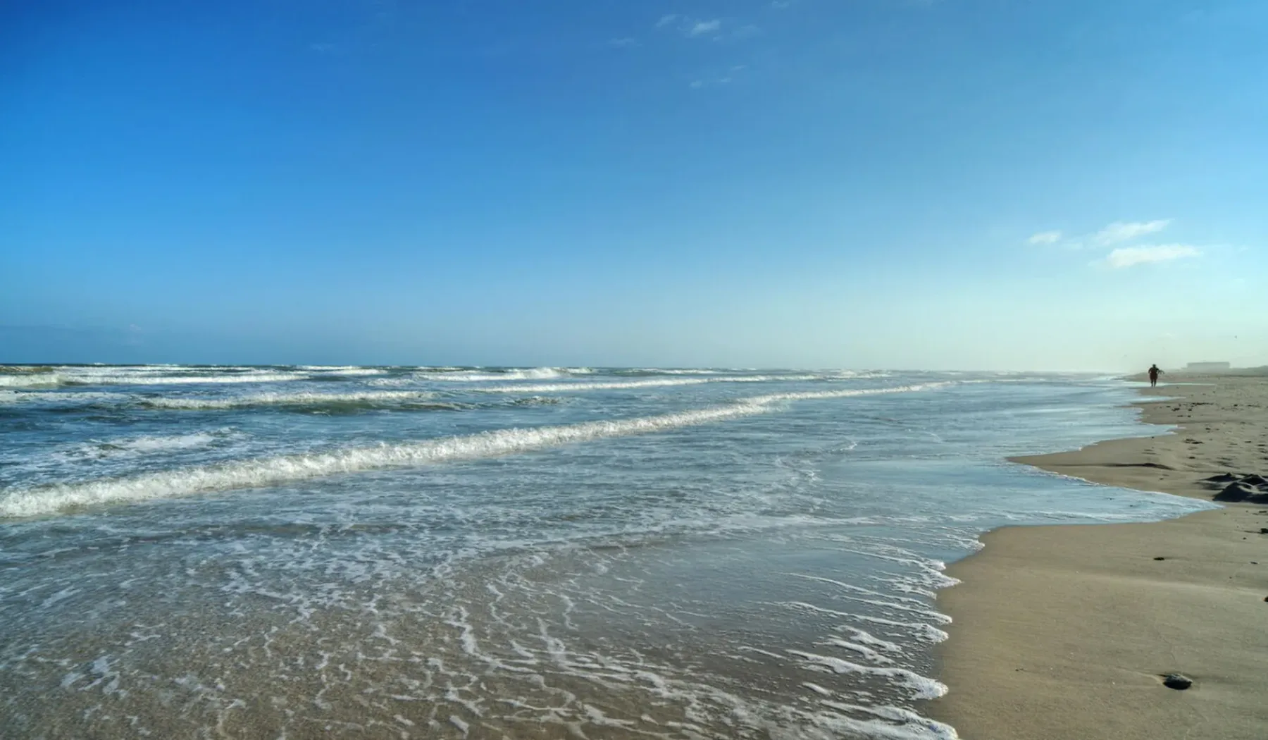 Una playa de arena con olas llegando a la orilla bajo un cielo azul despejado.