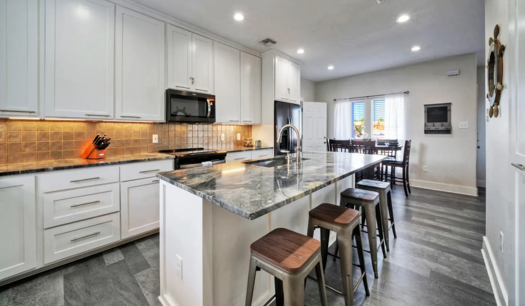 Una cocina luminosa con gabinetes blancos, una isla grande y asientos de barra.