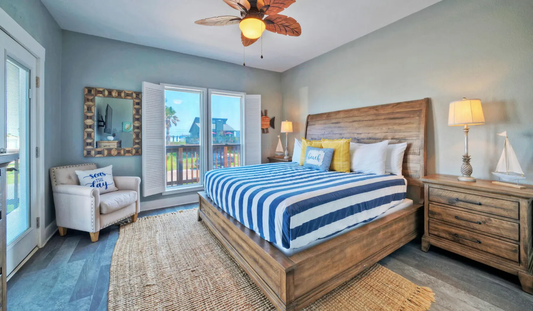 Un dormitorio con una cama de madera, ropa de cama a rayas azules y blancas y puertas corredizas de vidrio.