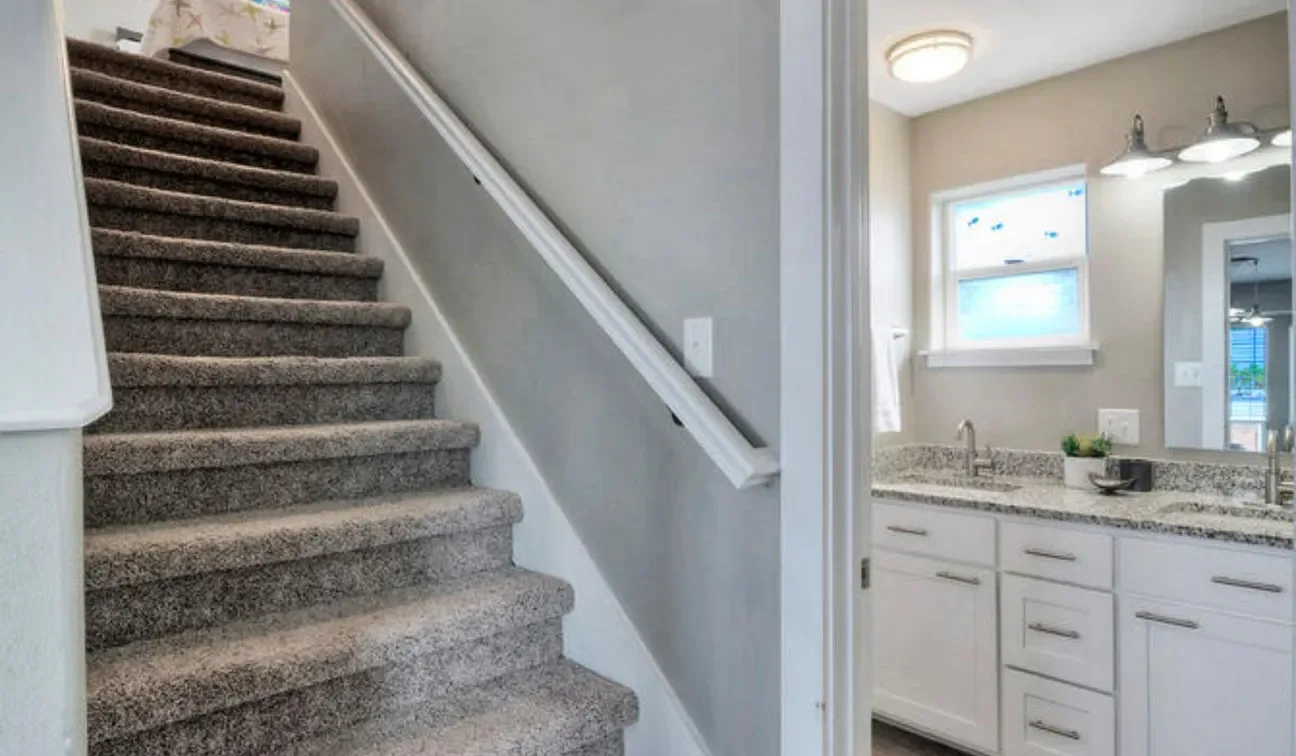 Una escalera alfombrada junto a un lavabo de baño y un espejo.