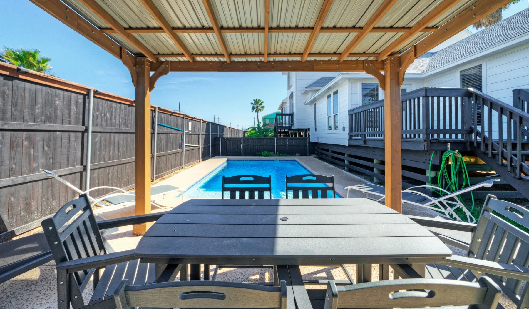 Una zona cubierta de comedor al aire libre da a una piscina junto a una casa.
