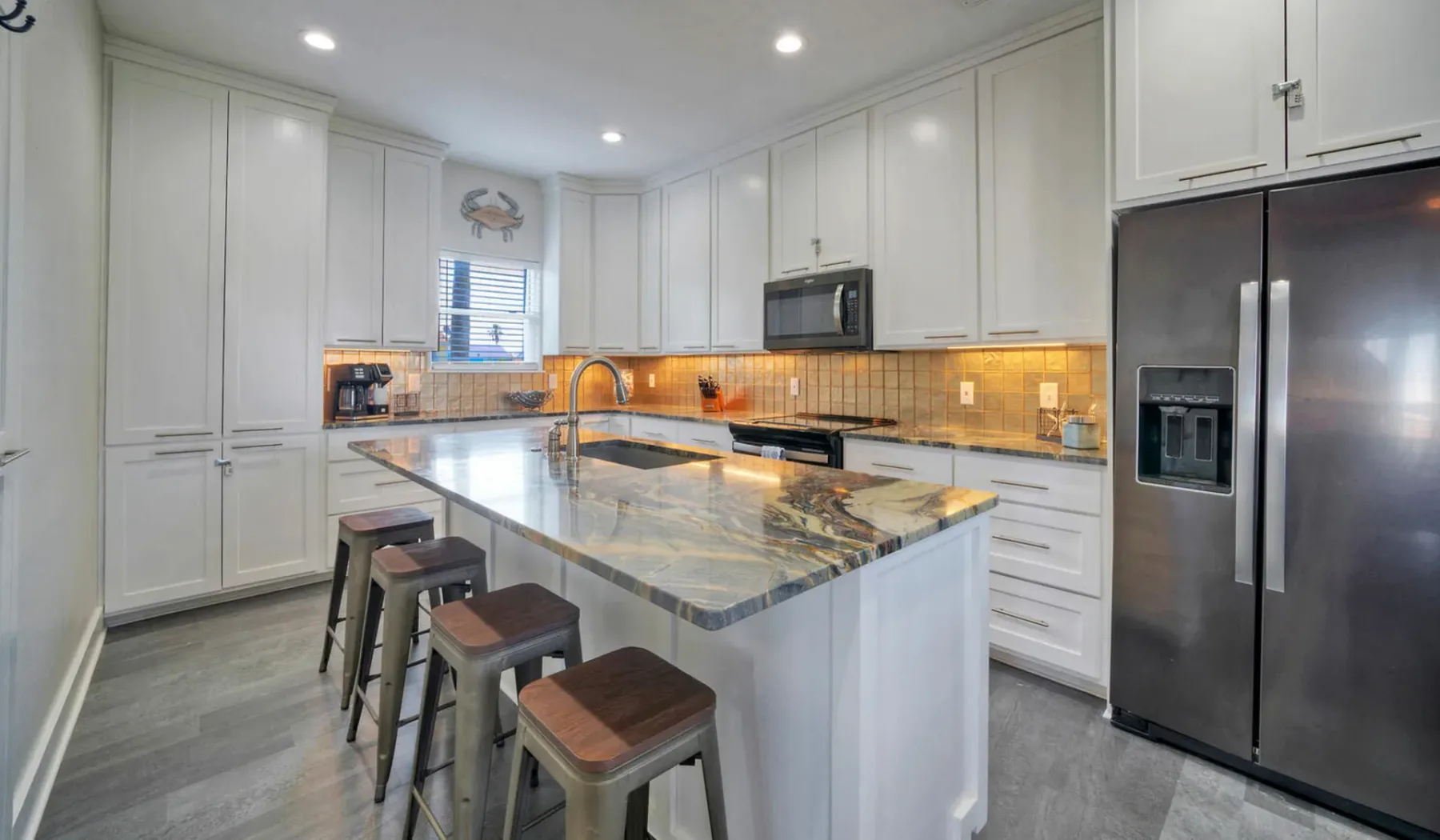 Una cocina luminosa con gabinetes blancos, una isla central y electrodomésticos de acero inoxidable.