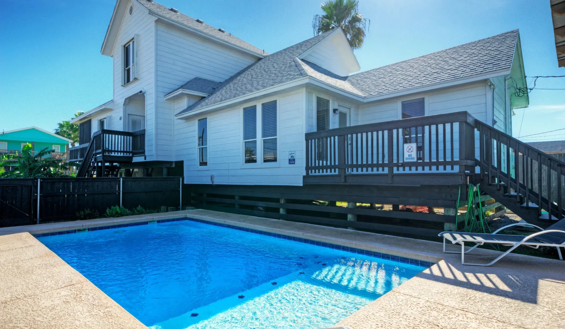 Una casa blanca está junto a una piscina azul y una terraza elevada.