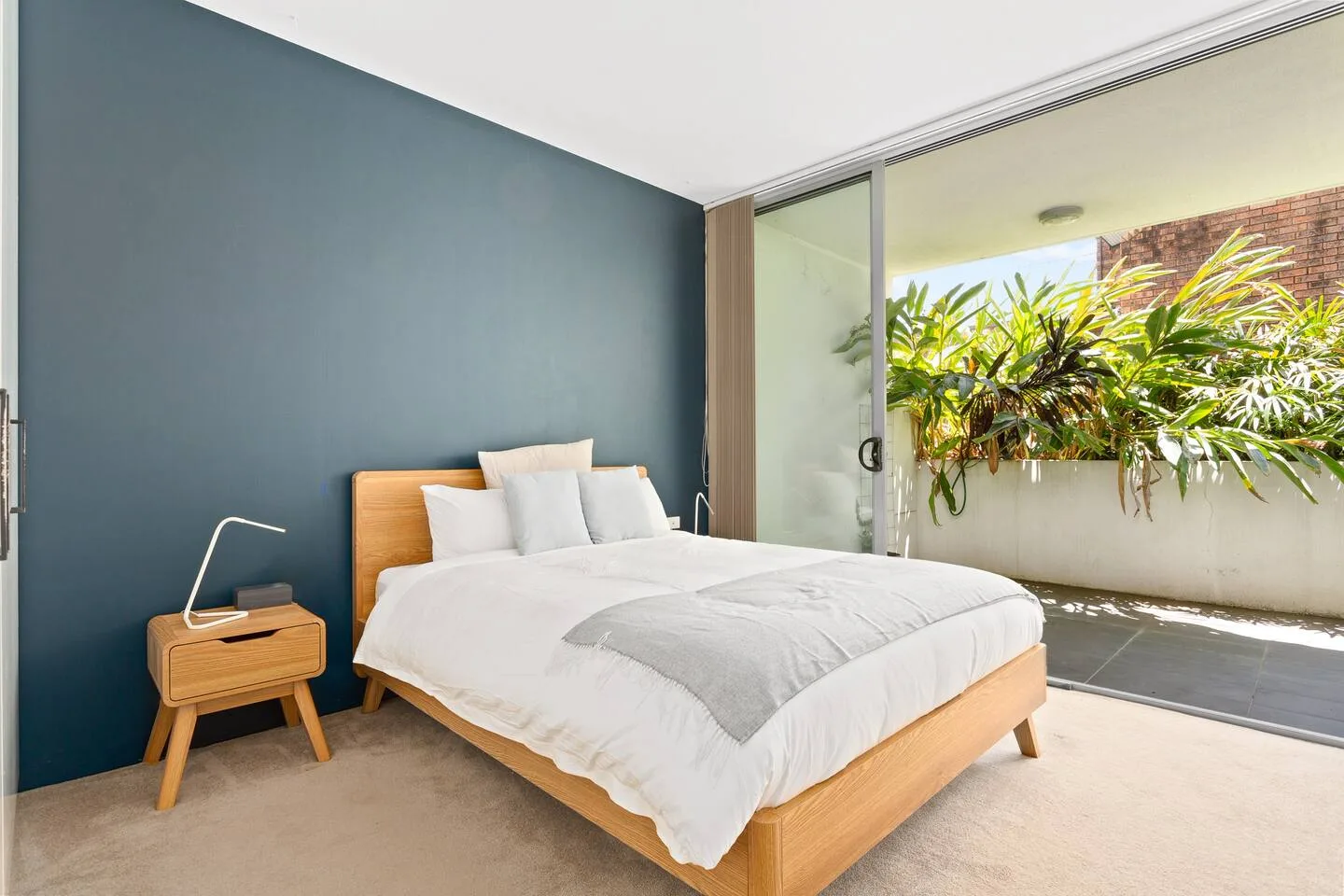 A bedroom with a neatly made bed beside a sliding glass door.