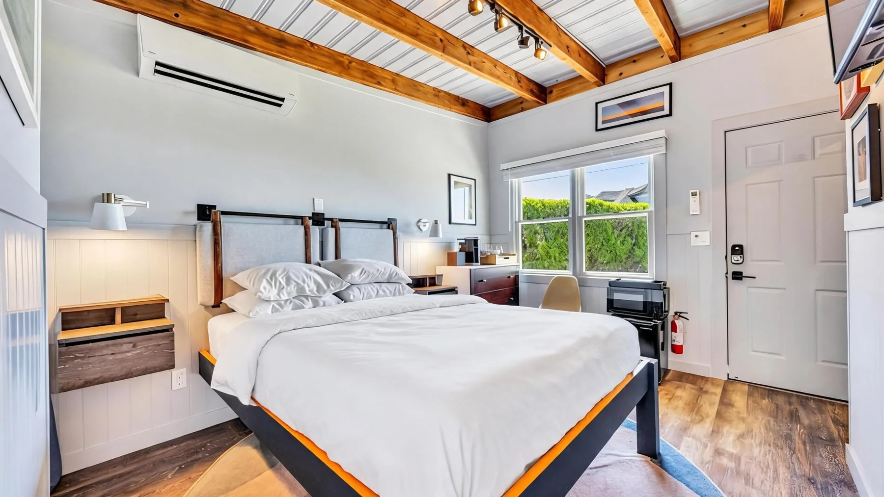 Un dormitorio luminoso con una cama grande, ventanas y vigas de madera expuestas en el techo.