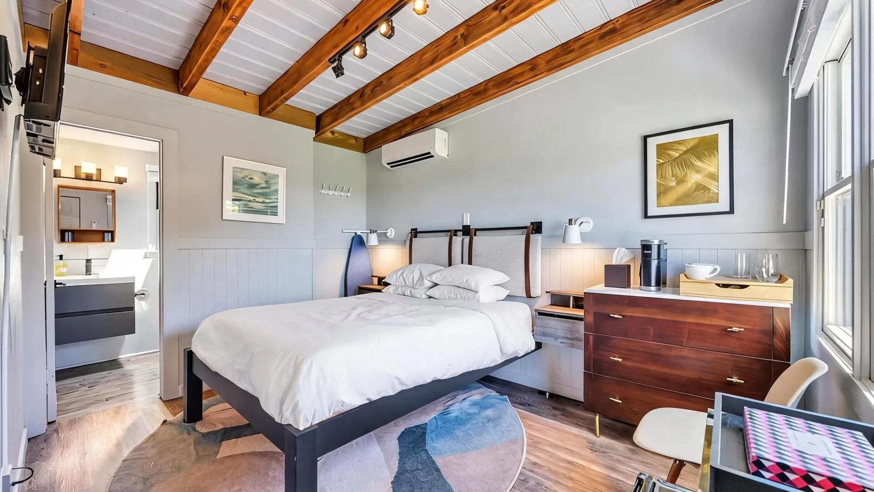A bedroom with a bed, wooden ceiling beams, and large windows.