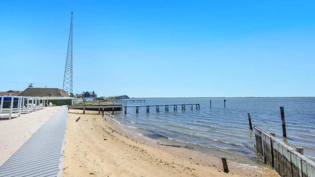 A sandy shoreline beside calm water, with a wooden walkway along the beach.