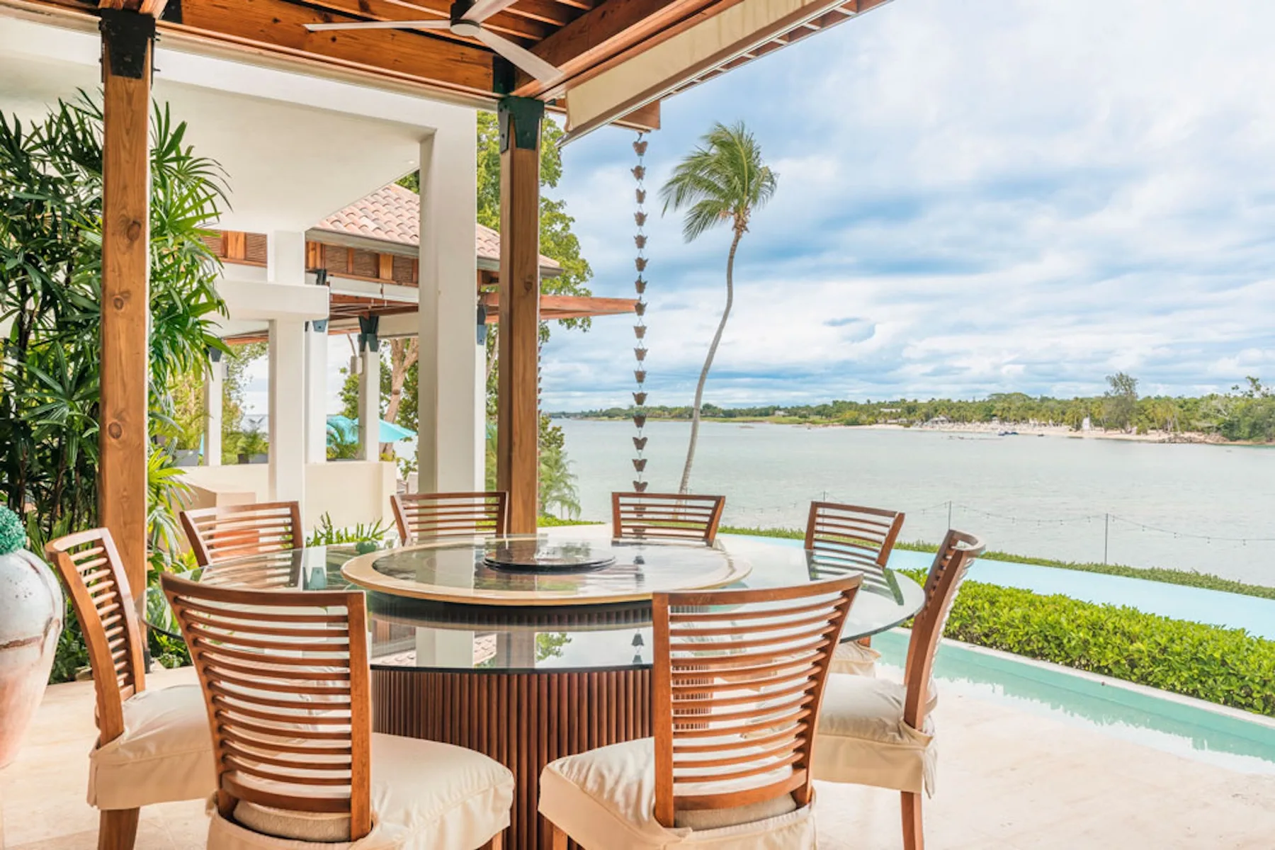 An outdoor dining area overlooks a pool and tropical waterfront.