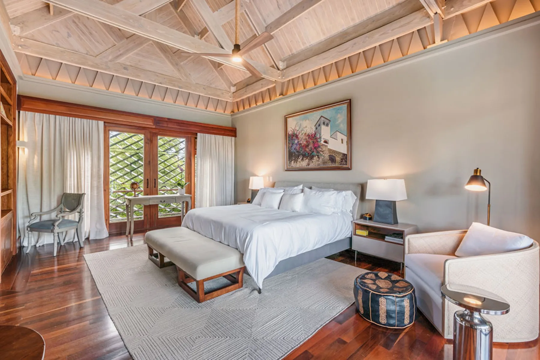 A bedroom with a large bed, seating, and a high exposed-beam ceiling.