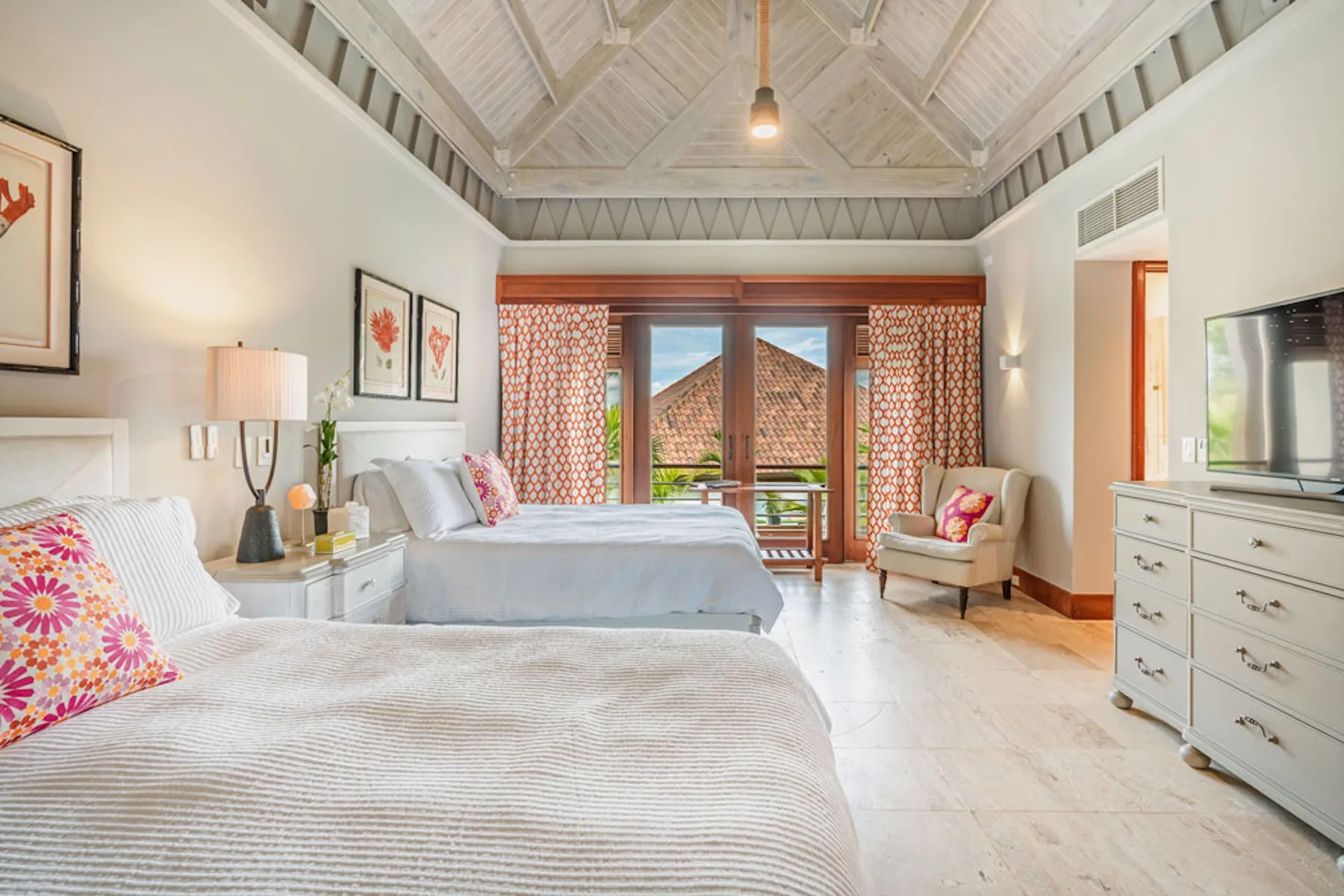 A bright bedroom with two beds, patterned curtains, and a high vaulted ceiling.