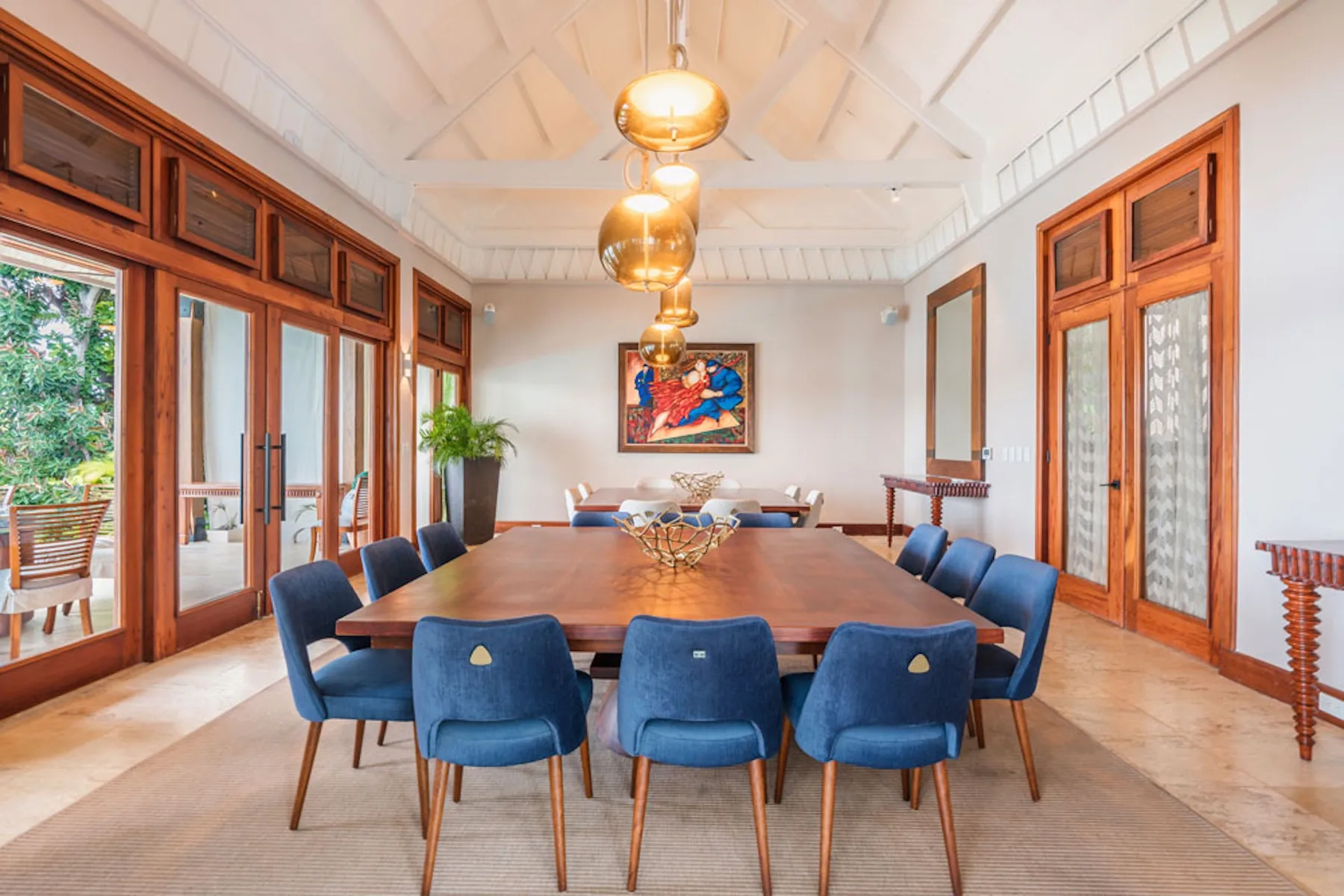 A dining room with a long table, blue seating, and pendant lights.