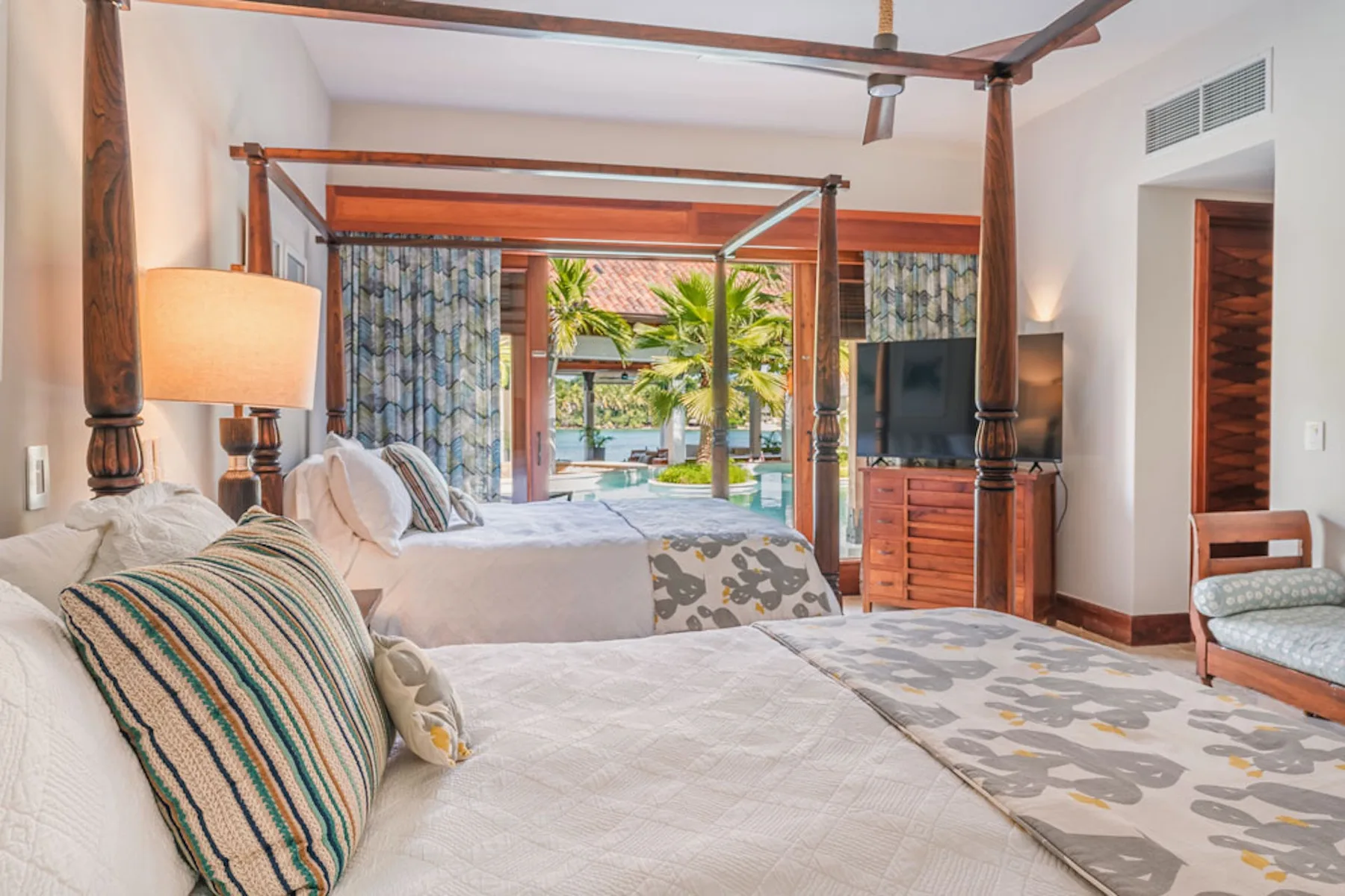 A bedroom with two beds, patterned bedding, and an open view to a garden.