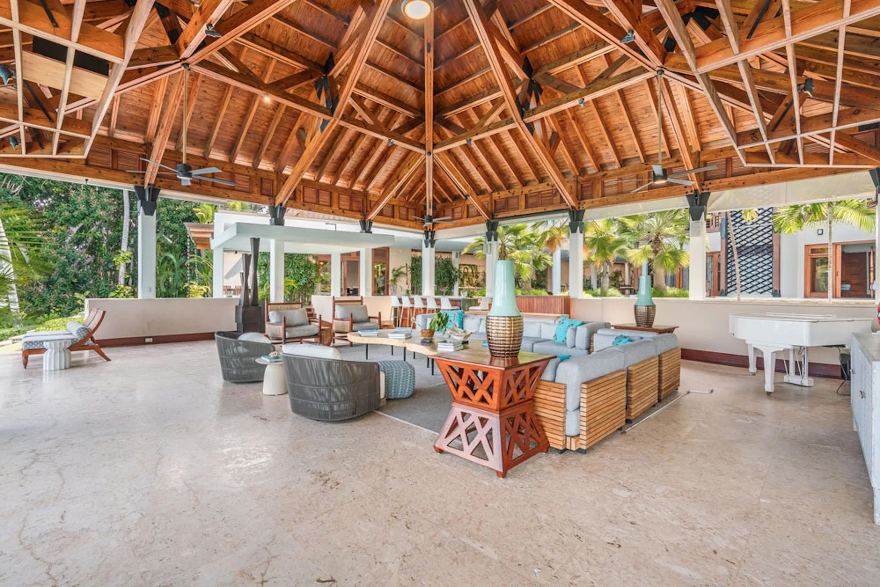 An open-air lounge beneath a wooden roof, furnished with seating and tables.