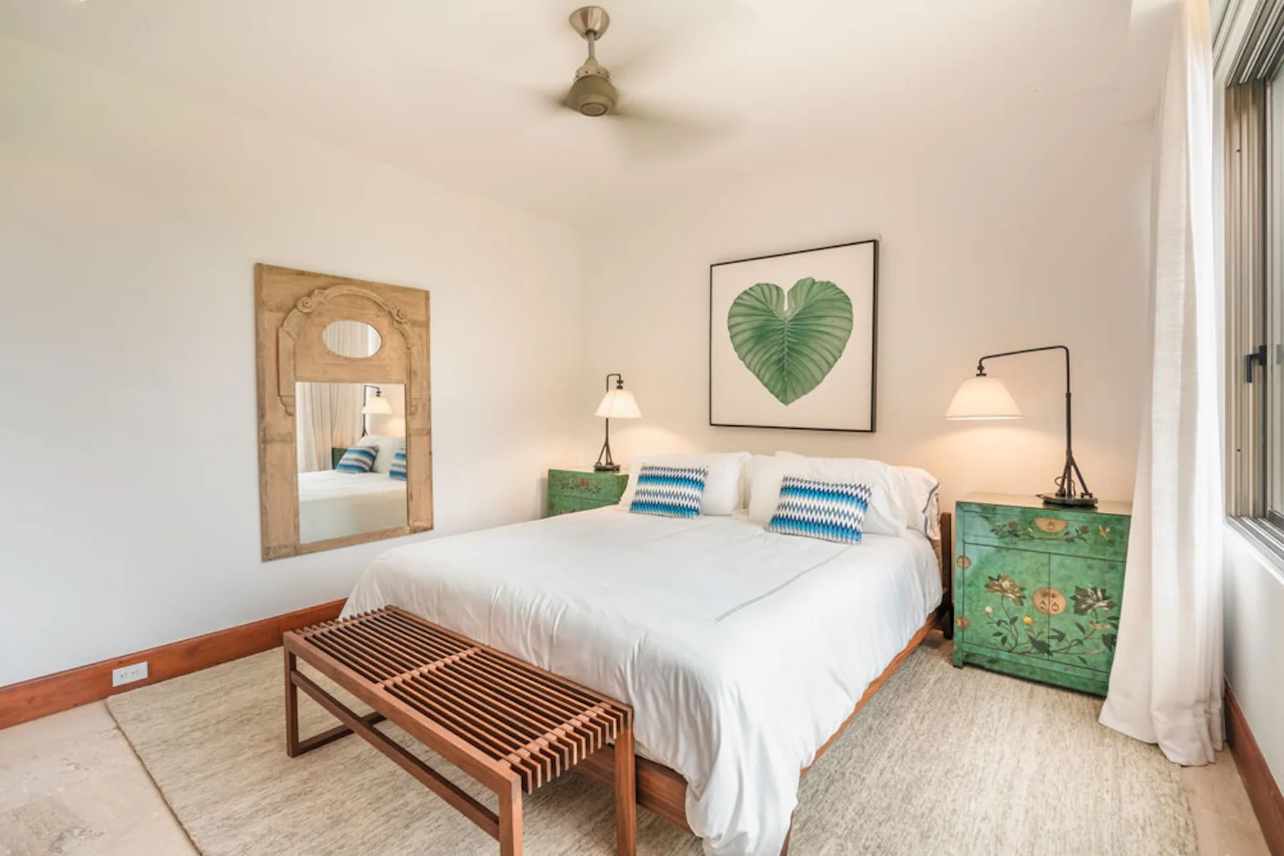 A bedroom with a neatly made bed and framed botanical artwork.