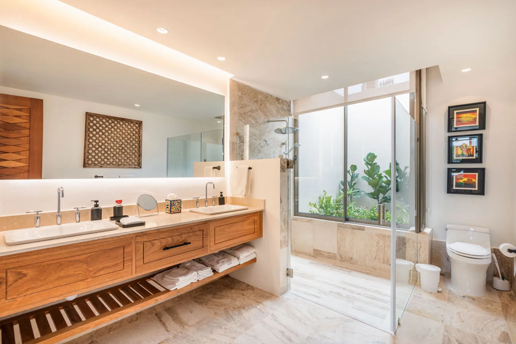 A bright bathroom with a long wooden vanity and glass shower.