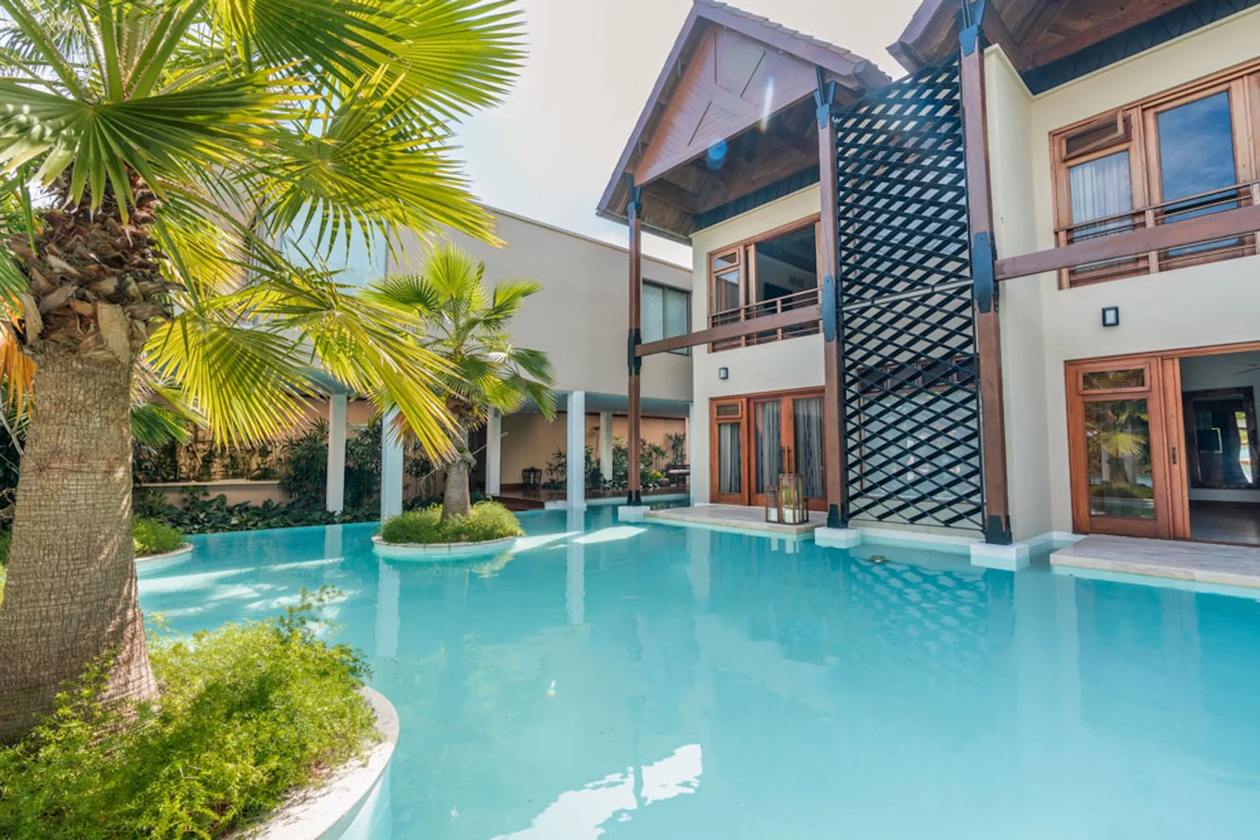 A turquoise swimming pool beside a modern building and palm trees.