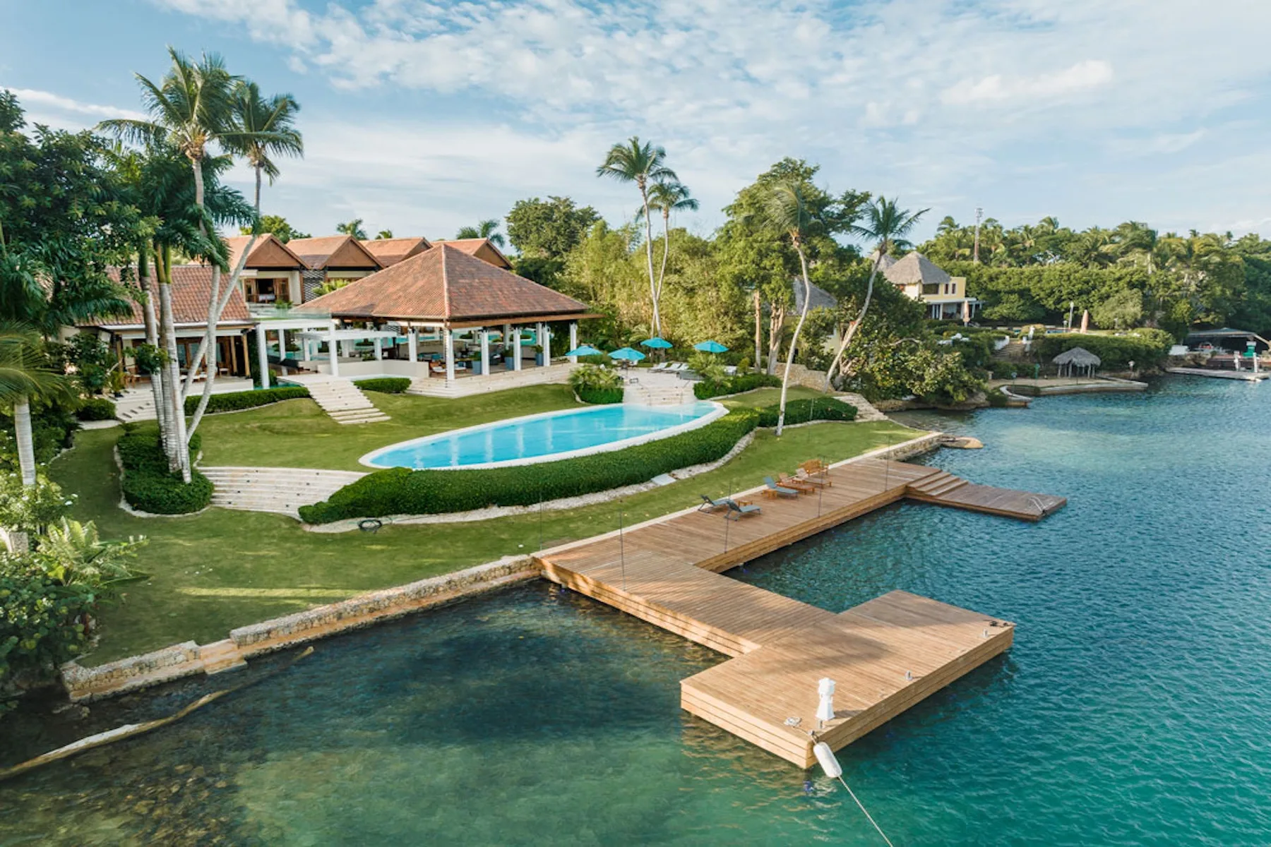A waterfront resort grounds with a swimming pool, palm trees, and wooden docks.