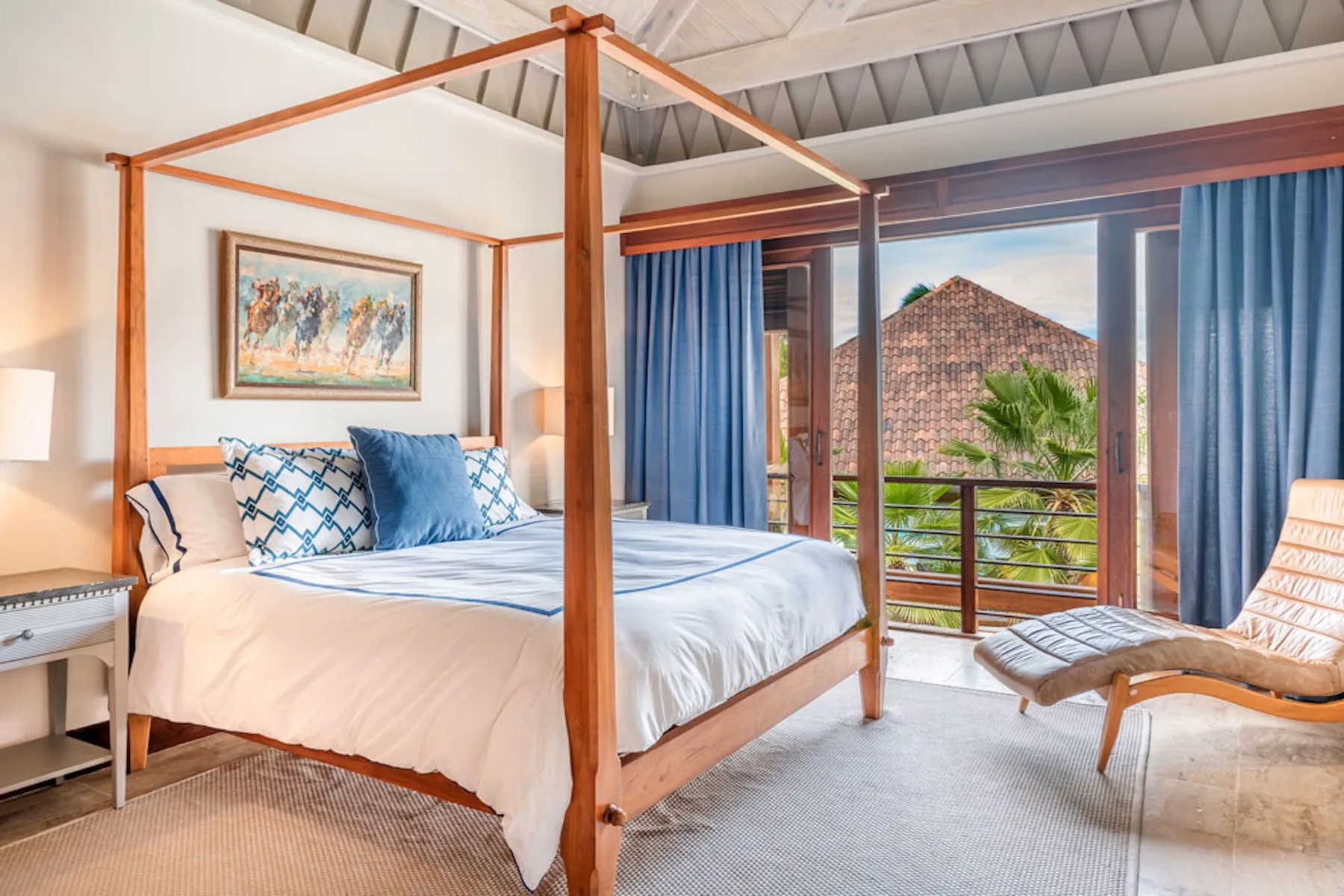 A bedroom with a four-post bed, blue curtains, and a balcony overlooking greenery.