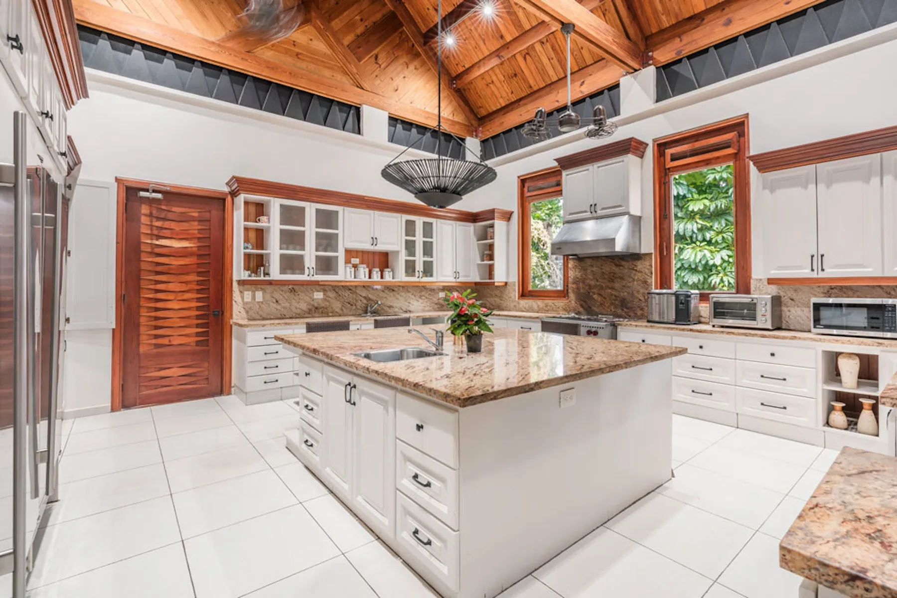 A spacious kitchen with a central island, white cabinetry, and a wood ceiling.