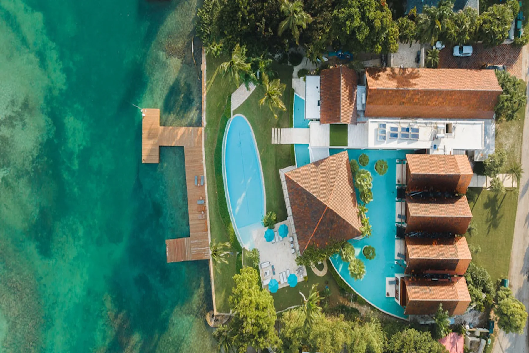 An aerial view of a seaside resort with pools and a wooden dock.