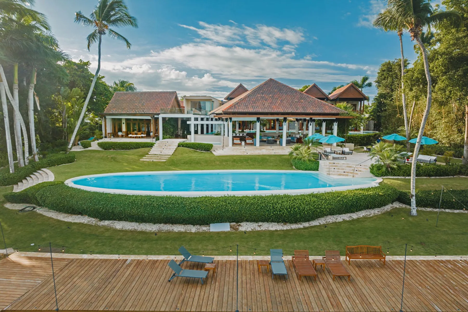 A tropical resort scene with a swimming pool, landscaped lawn, and palm trees.