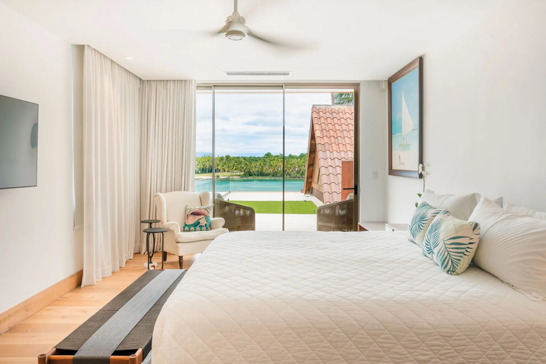 A bright bedroom with a large bed and sliding glass doors overlooking greenery and water.