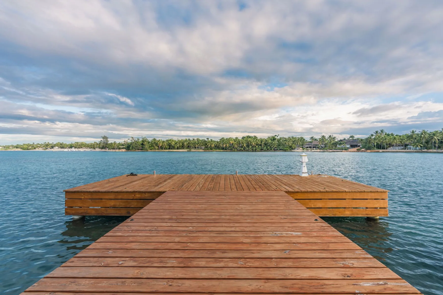 A wooden dock extends over calm blue water beneath a cloudy sky.