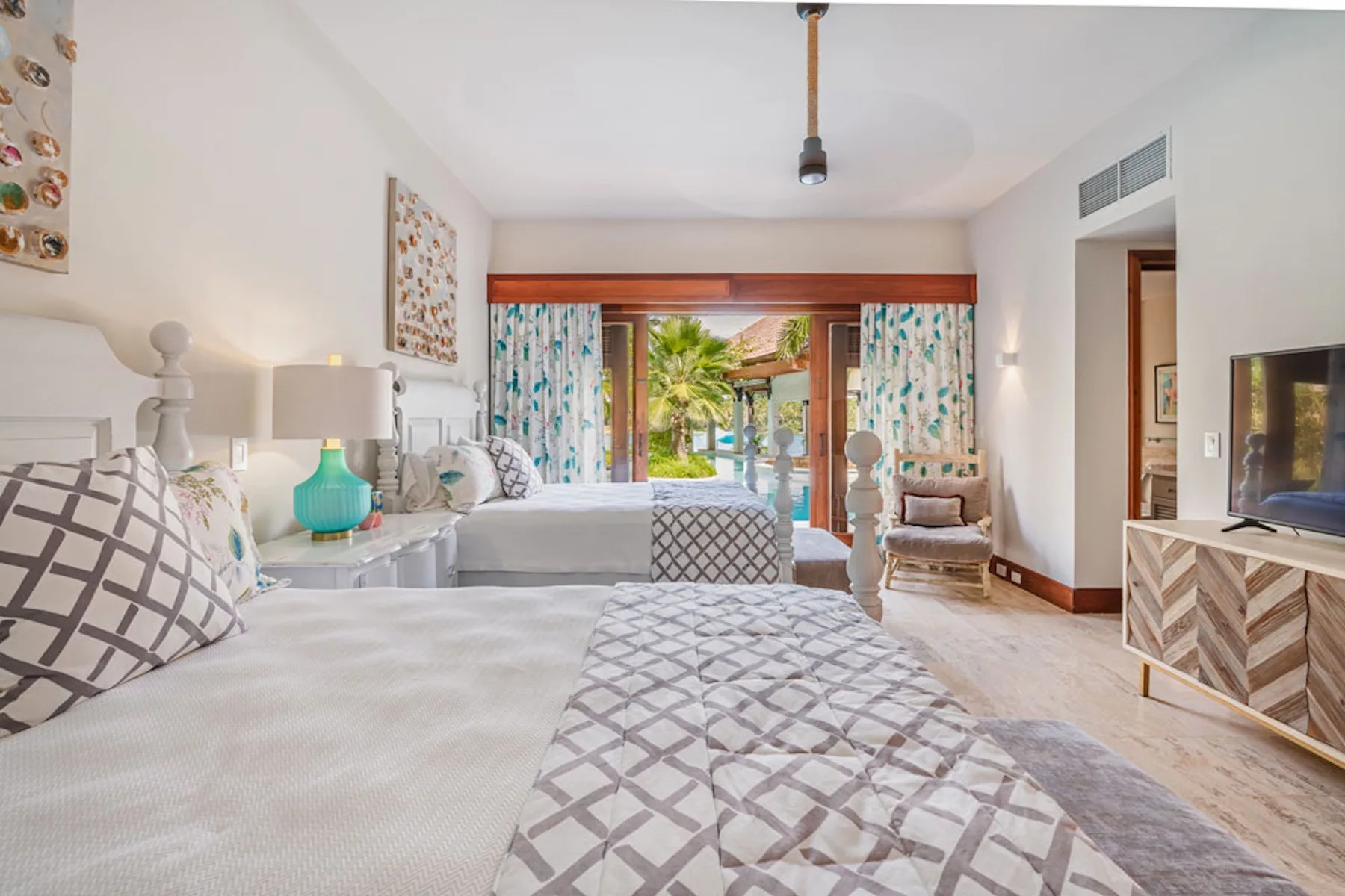 A bright bedroom has patterned bedding and glass doors opening onto a balcony.
