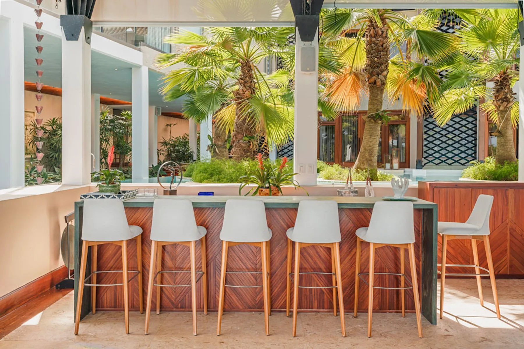 An outdoor bar with a long counter and seating beneath palm trees.