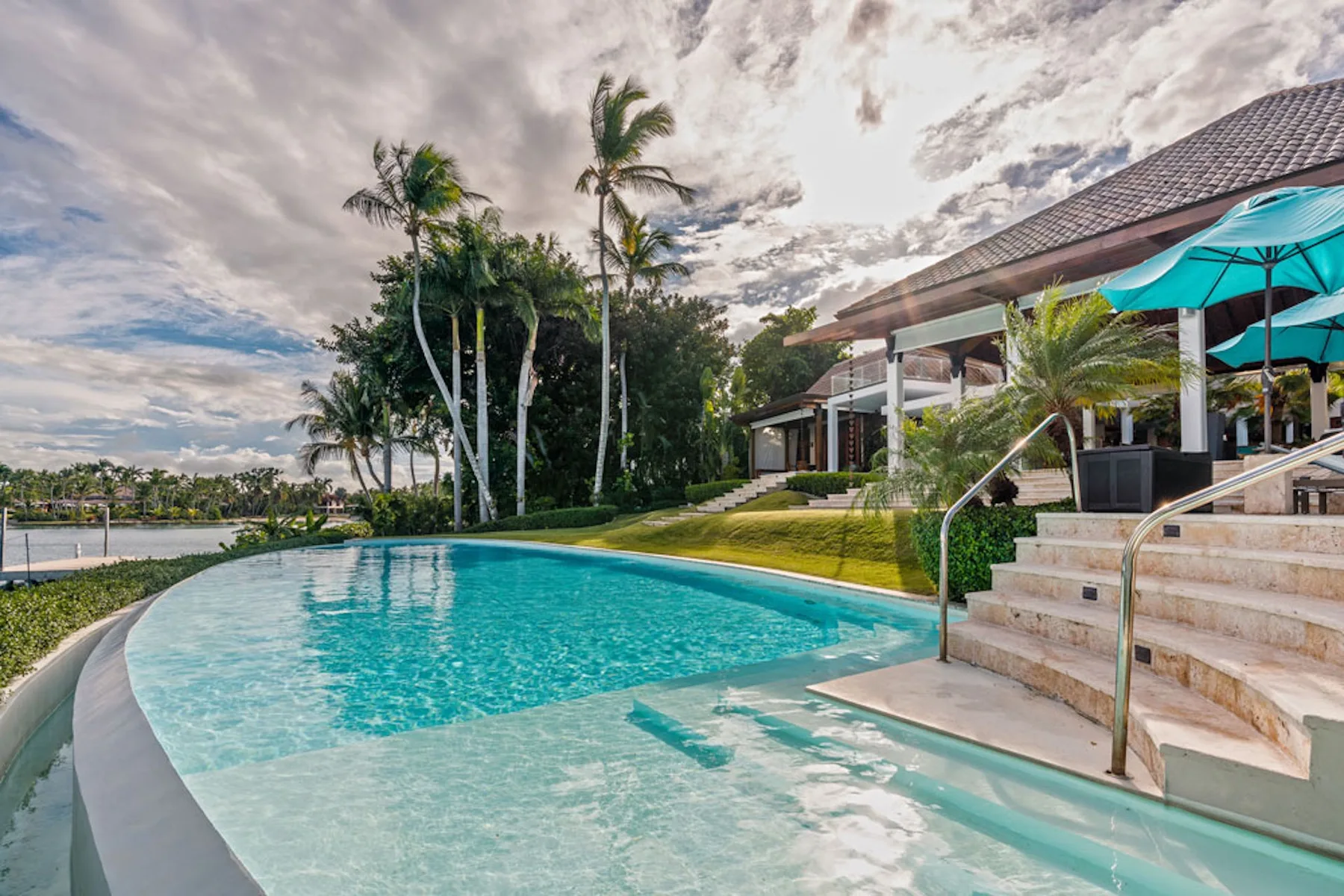 Outdoor swimming pool beside a landscaped property, with palm trees and a shaded seating area.