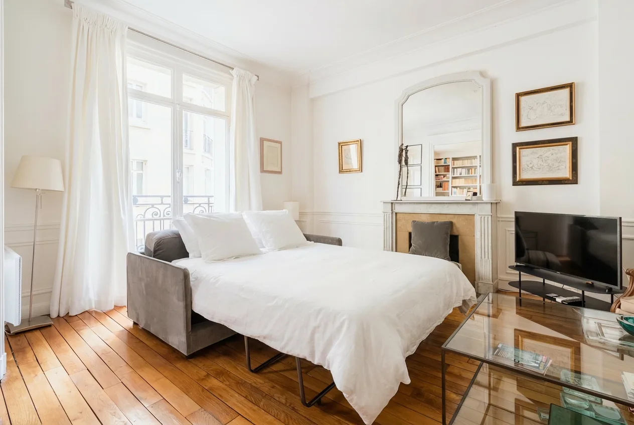 Un dormitorio luminoso con una cama blanca, ventanas altas y una chimenea.