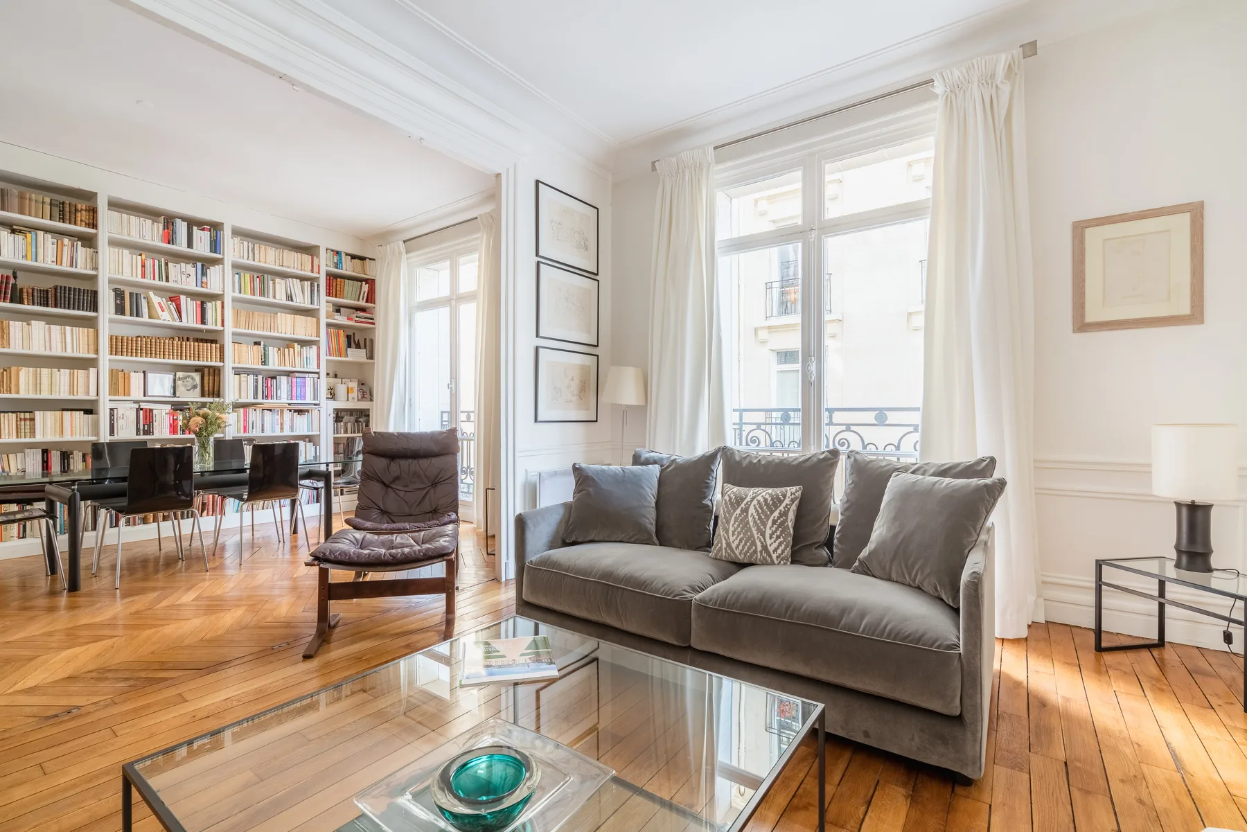 Una sala luminosa con asientos grises, una mesa de centro de vidrio y ventanas altas.