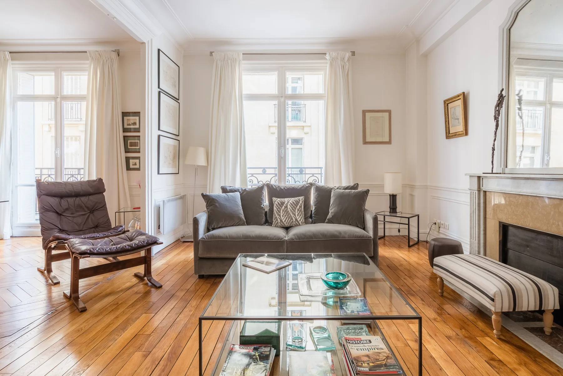 Una sala de estar luminosa con asientos, una mesa de centro de vidrio y ventanas altas.