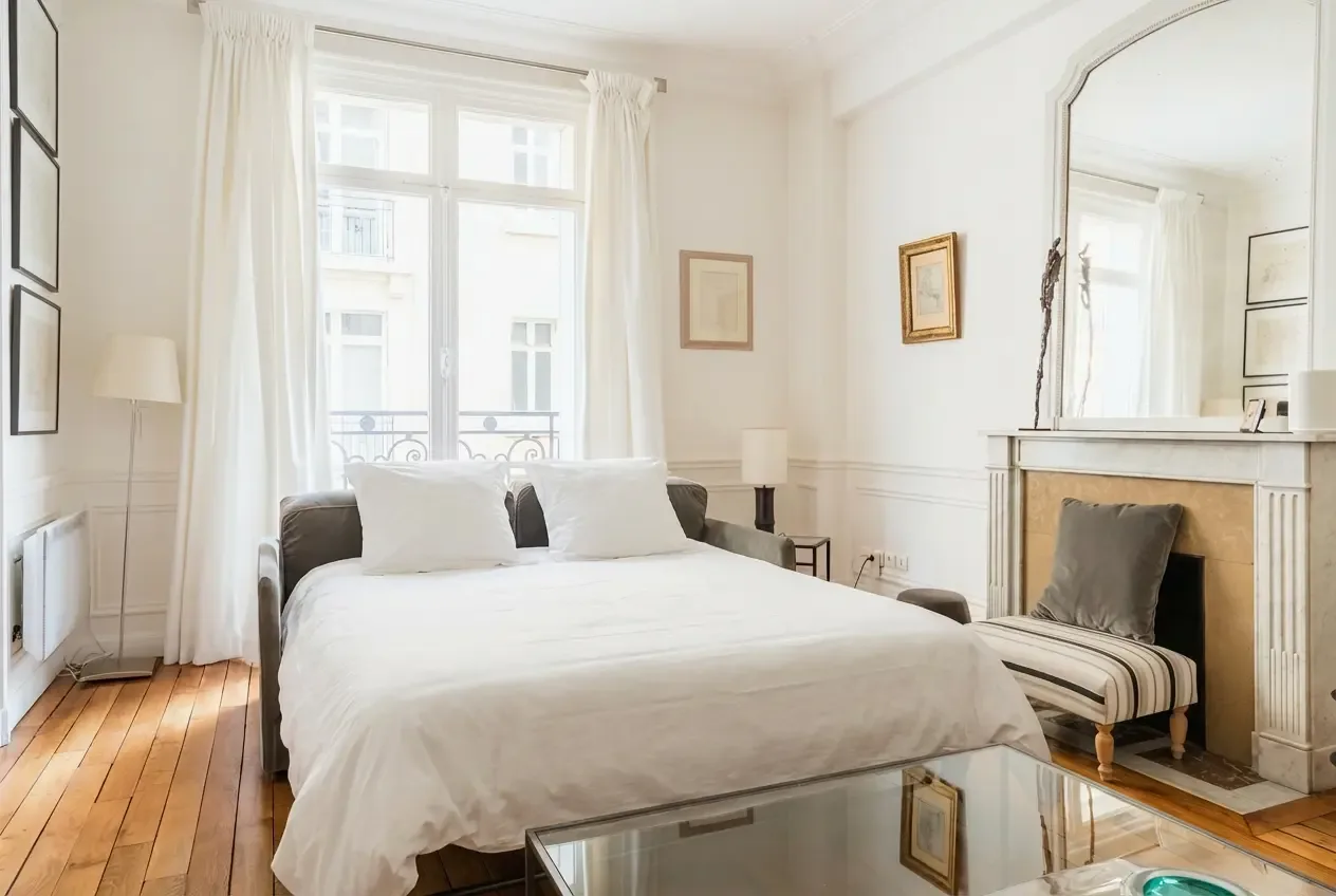 Un dormitorio luminoso con una cama grande junto a ventanas altas.
