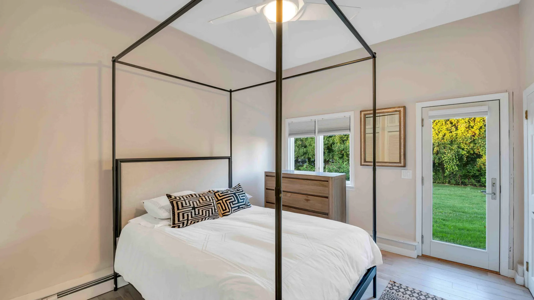 Un dormitorio luminoso con una cama con dosel y puertas de vidrio hacia el jardín.