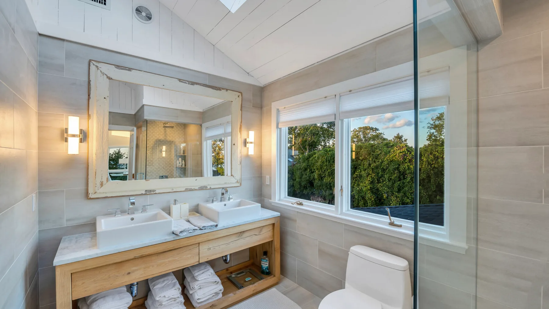 Un baño luminoso con tocador doble, un espejo grande y ventanas con vistas a la vegetación.