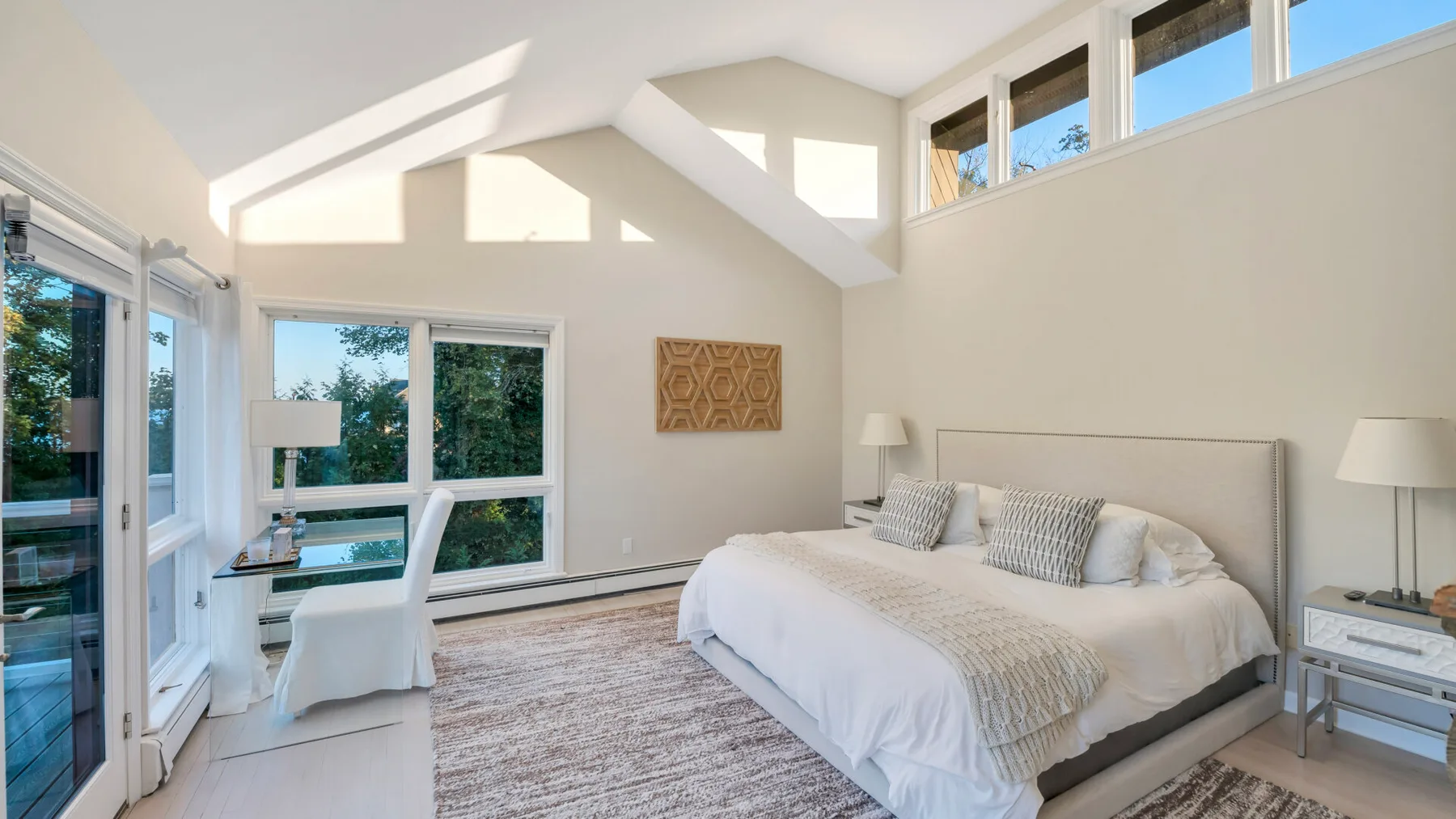 Un dormitorio luminoso con una cama junto a grandes ventanas con vistas a la vegetación.