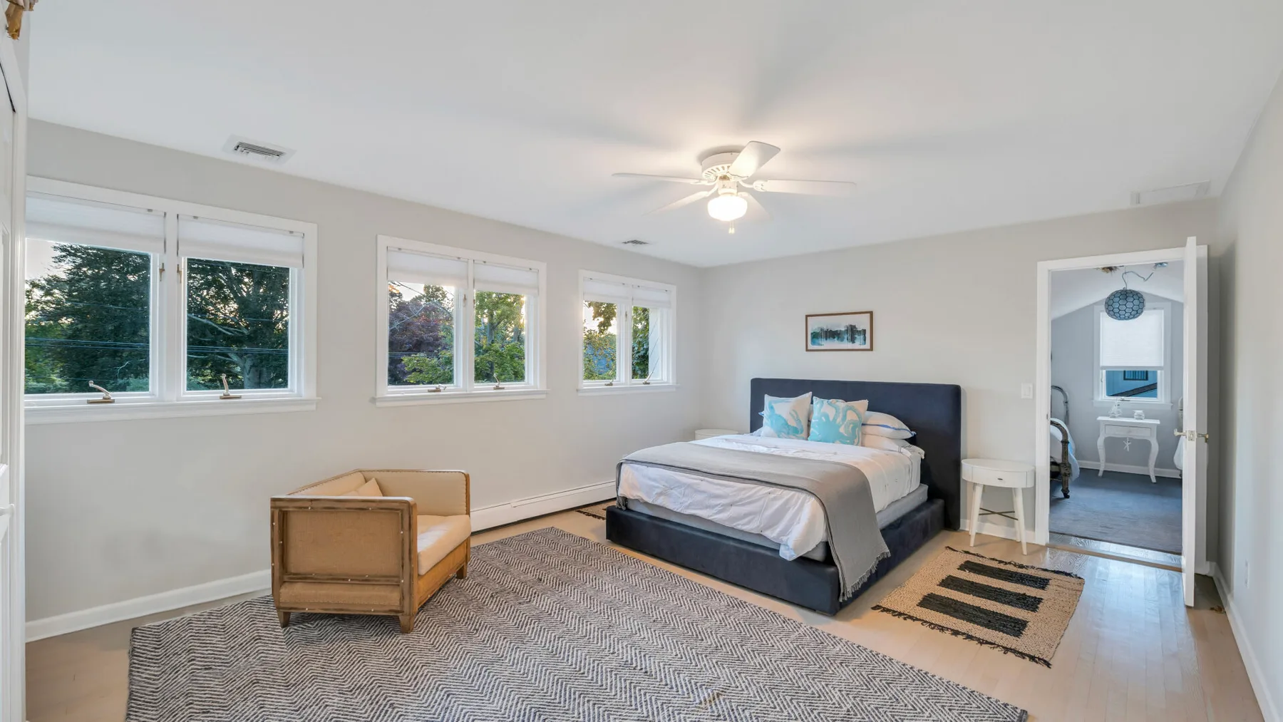 Dormitorio luminoso con una cama, varias ventanas y una pequeña zona de estar.