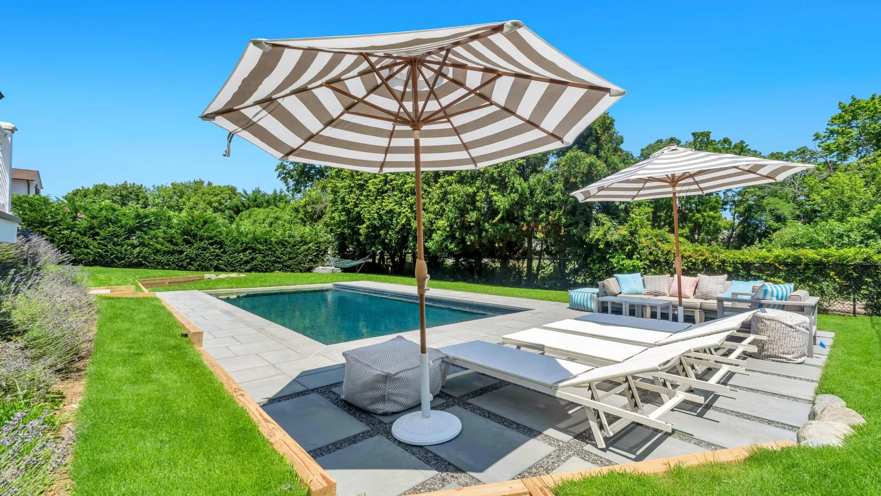 Zona de piscina al aire libre con asientos reclinables y grandes sombrillas a rayas.